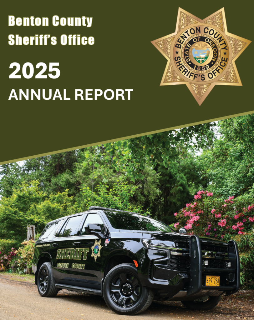 A black Benton County Sheriff's Office SUV parked on a road surrounded by green trees and flowering bushes.